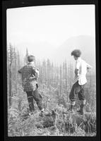 [Two men viewing mountains with an area damaged by a forest fire in the foreground]