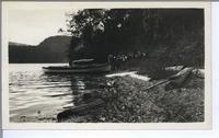 [Small boat and group of people on the shore of a lake or bay in an unknown location]