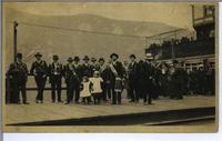 [Group of people standing on a wooden sidewalk in an unknown location]