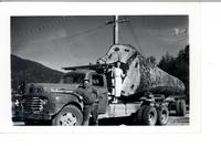 [Woman next to a large log on a logging truck]