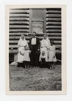 [Photograph of a man, two women and three children outside a log house, c. 1940s]