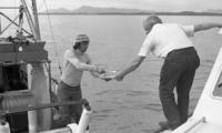 [Two men exchanging papers on two side by side fishing boats]