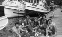 [Group photograph of seven men on a dock with a soccer ball in front]