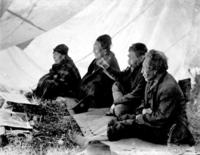 Group of two Kwakiutl men and two women sitting on ground in a tent