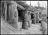 House front with four large carved poles, images of whales