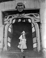 Ne-kar-at-see, portrait of a Kwakiutl woman standing in the doorway of a house