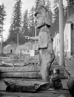 Girl sitting near totem pole, canoe and button blanket