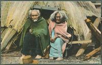 Elderly First Nations man and woman sitting outside hut